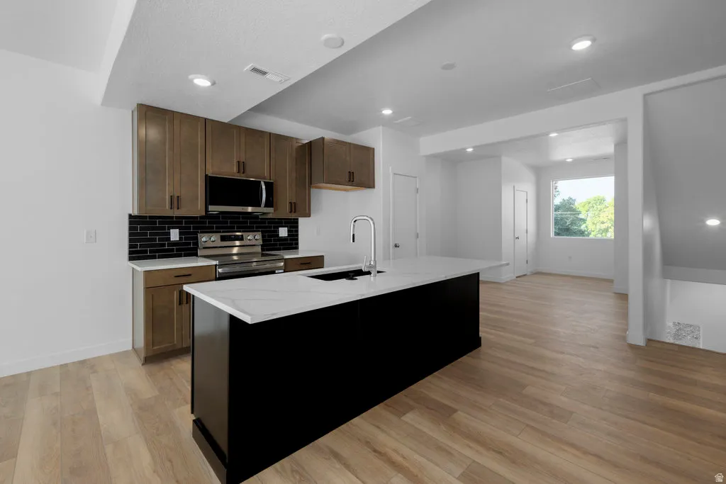 Modern kitchen featuring a large black island with a white quartz-finish countertop, stainless steel appliances, wood-finish cabinetry, and a black subway tile backsplash