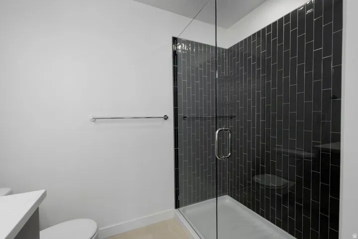 Full-glass shower enclosure with dark vertical subway tile surround, integrated shower bench, and a chrome towel bar