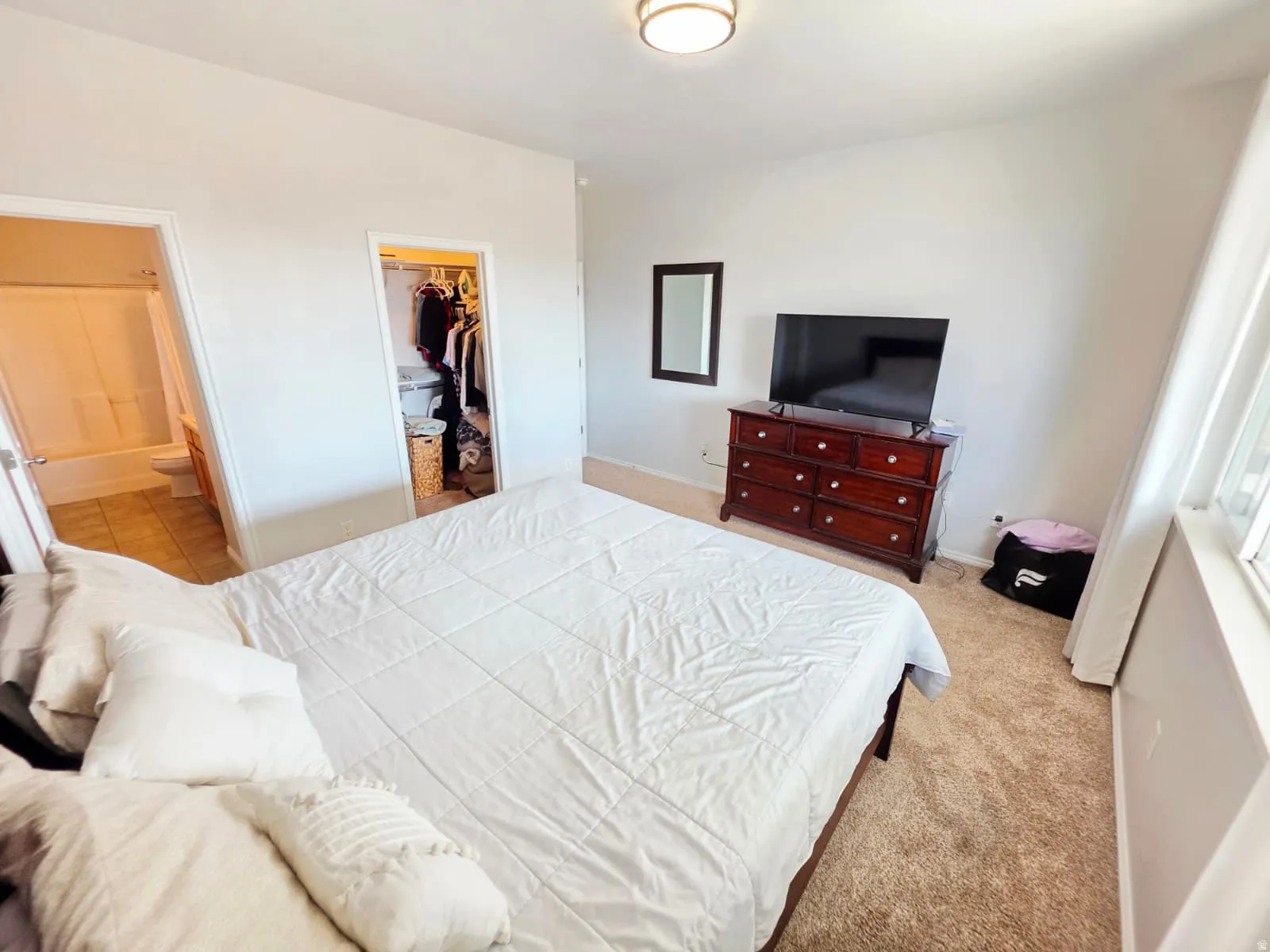 Bedroom featuring neutral-toned walls, carpeted flooring, a walk-in closet, and a bathroom with a tub/shower combination and tiled flooring