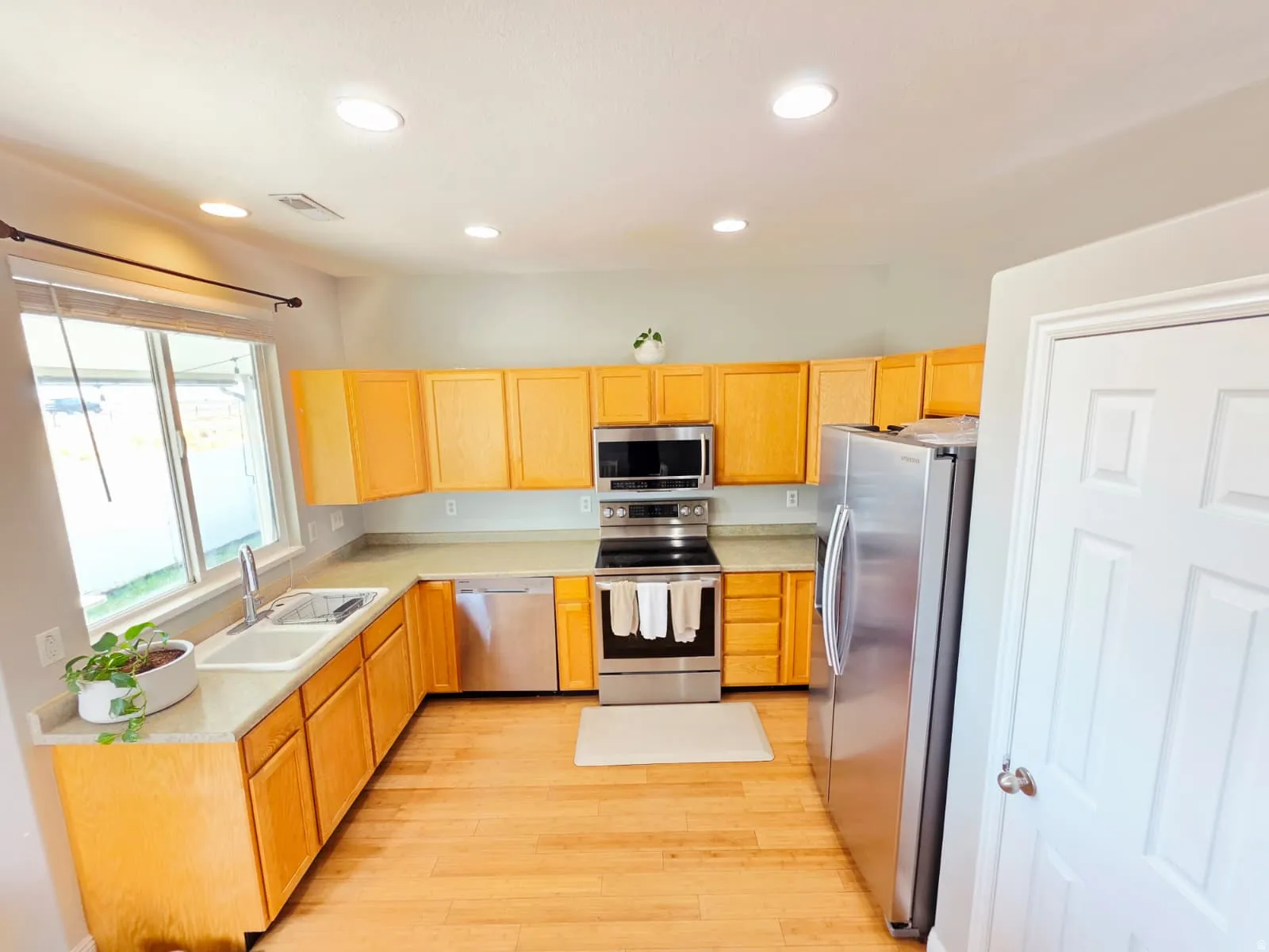 Kitchen featuring wood-finish cabinetry, stainless steel appliances, light-toned countertops, a stainless steel sink, and wood-finish flooring