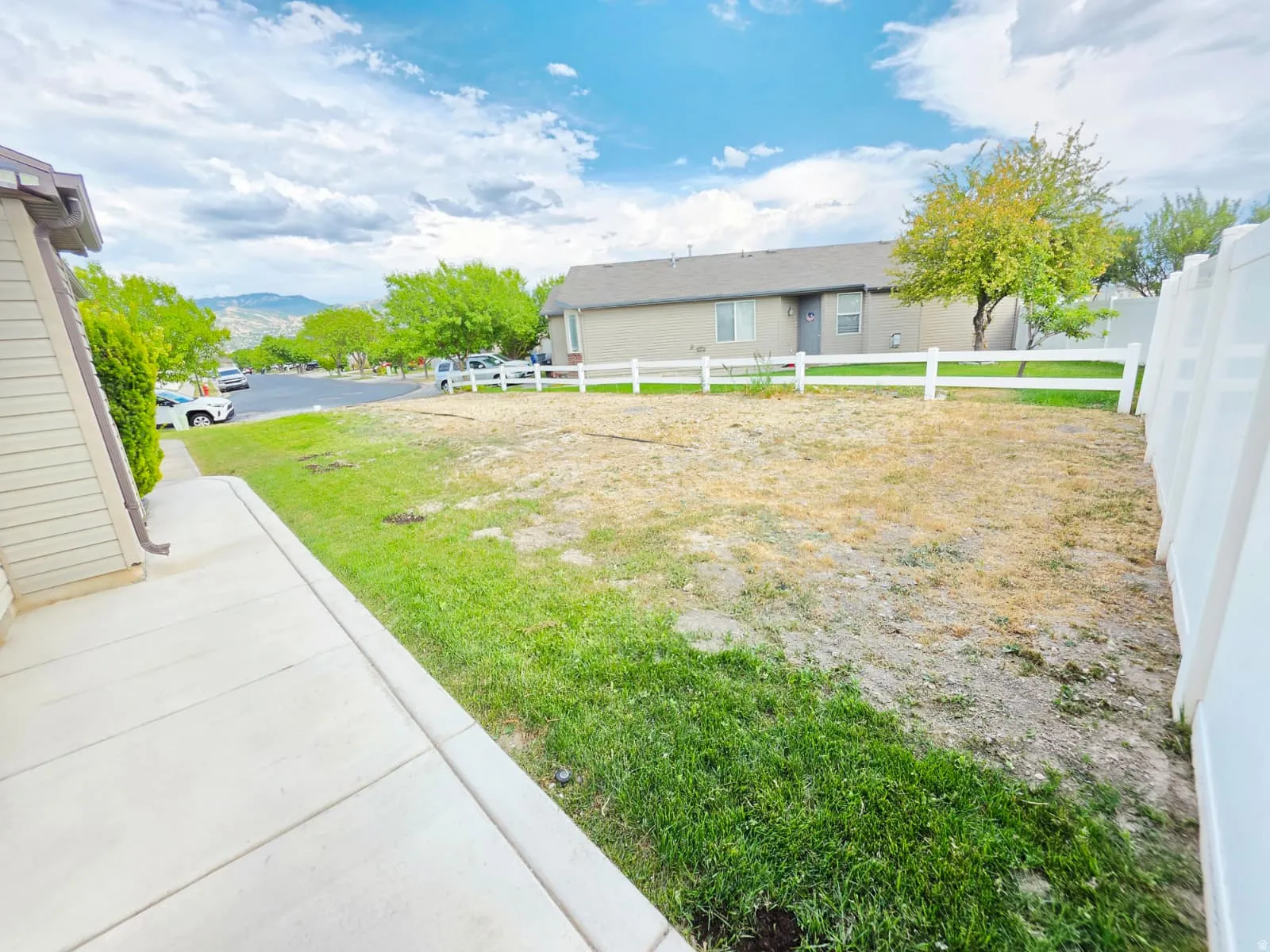 Expansive outdoor area featuring a white vinyl privacy fence, a white picket fence, and a concrete pathway