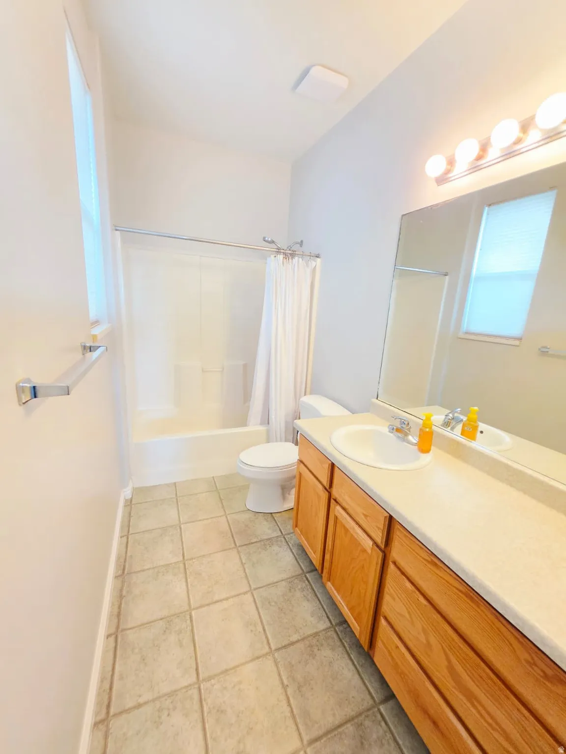 Bathroom featuring a single vanity with wood-finish cabinetry and a light-toned countertop, a shower-tub combination, and tiled flooring