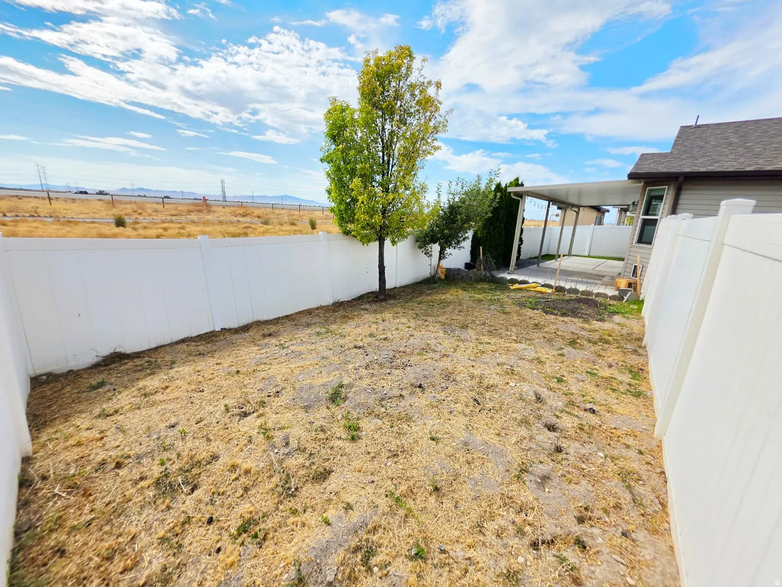 Spacious backyard with a white privacy fence, mature trees, and a covered patio area with a concrete surface