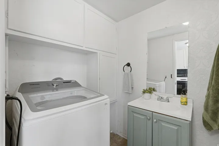 Dedicated utility space featuring overhead white cabinetry, a built-in shelf, a single-sink vanity with a light green cabinet, and a wall-mounted mirror