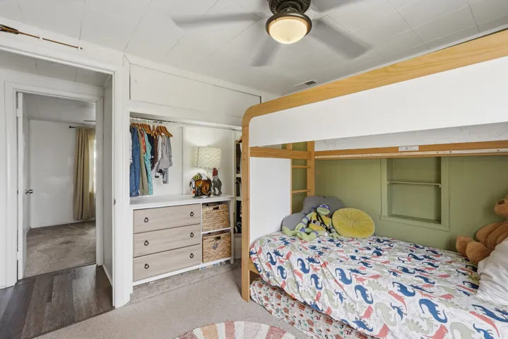 Bedroom featuring a built-in bunk bed, an integrated closet system with drawers and shelving, wood-finish flooring at the doorway, carpeted flooring, and an overhead ceiling fan