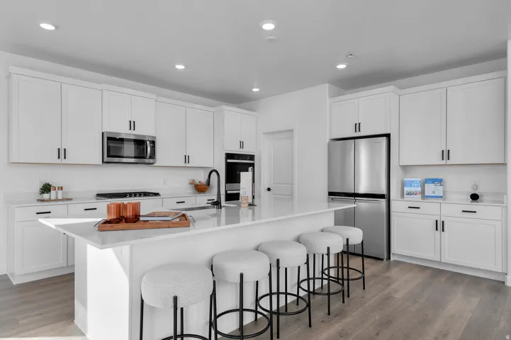 Kitchen featuring an expansive island with seating, white shaker cabinetry, stainless steel appliances, a built-in wall oven, and wood-finish flooring