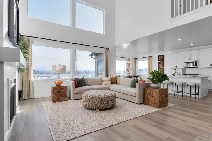 Open-concept living area featuring a two-story ceiling with high transom windows, wood-finish flooring, and a modern fireplace with a white mantel
