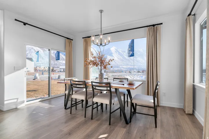 Open-concept dining area featuring wood-finish flooring, a modern linear chandelier, crown molding, and expansive windows