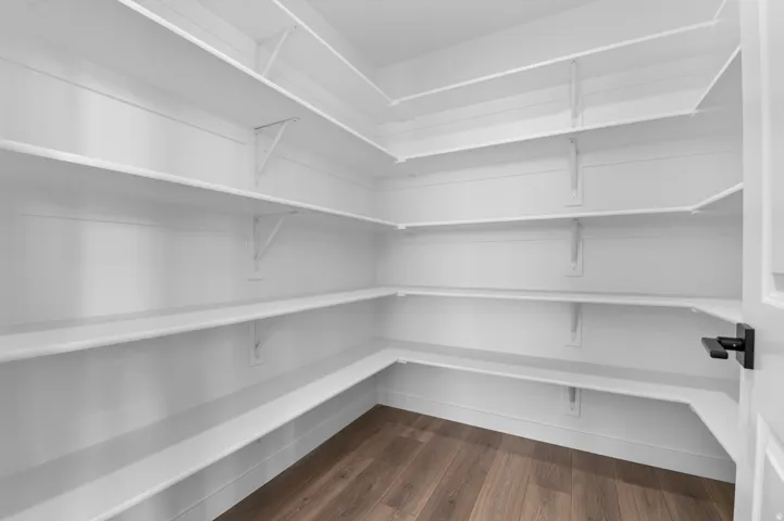 Walk-in pantry featuring extensive white shelving, wood-finish flooring, and a modern black door handle