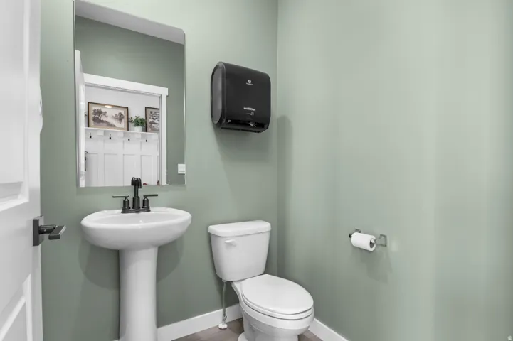 Pedestal sink with a matte black faucet, wall-mounted mirror, and white toilet