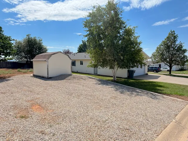 Gravel parking area featuring a detached storage shed with a gambrel roof and a concrete driveway