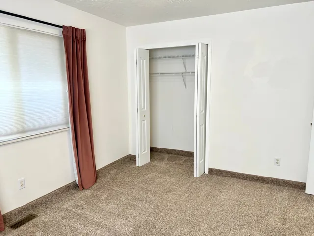 Carpeted interior room featuring a window with cellular shades, a bi-fold closet with wire shelving, white painted walls, and dark baseboard trim
