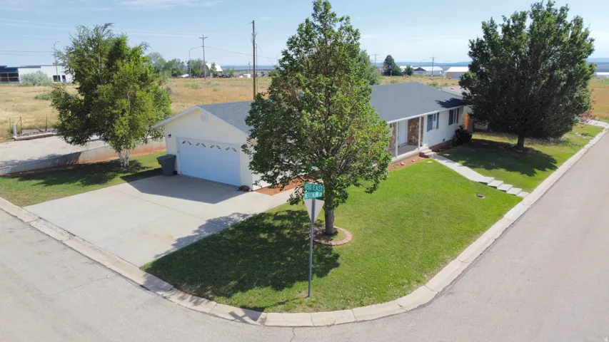 Ranch-style residence featuring a light-colored exterior, an attached two-car garage, a concrete driveway, and a well-maintained lawn with mature trees