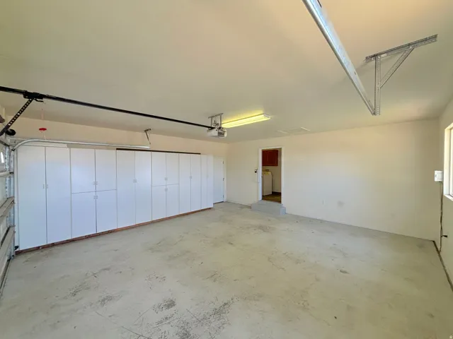 Spacious garage featuring extensive built-in white cabinetry, concrete flooring, overhead fluorescent lighting, a window, and an interior door