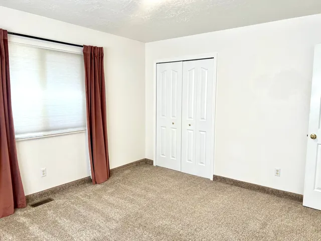 Bright room featuring light-colored walls, carpet flooring, a window with blinds, and white bi-fold closet doors