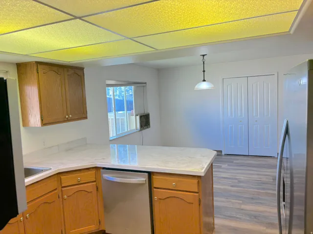 Kitchen featuring wood cabinetry, light-toned countertops, and a stainless steel dishwasher