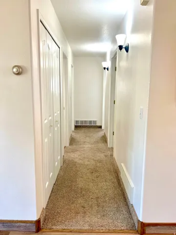 Hallway featuring light beige carpeting, white walls, and wood-finish baseboards