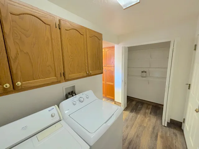 Functional laundry space featuring wood-finish flooring, overhead cabinetry, and an adjacent pantry with wire shelving