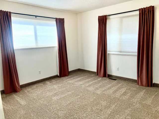 Carpeted room with white walls and two windows featuring blinds and drapes
