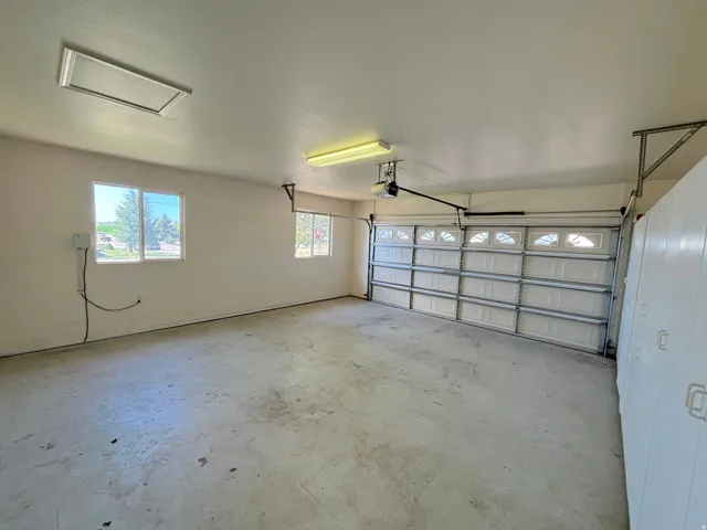 Spacious garage featuring a concrete floor, two windows providing natural light, a white paneled garage door with decorative glass inserts, an automatic garage door opener, and built-in white cabinetry