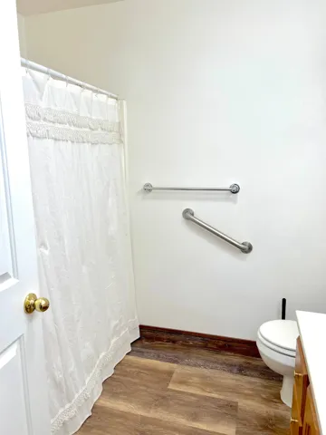 Bathroom featuring wood-finish flooring, white walls, and a shower area with a white curtain