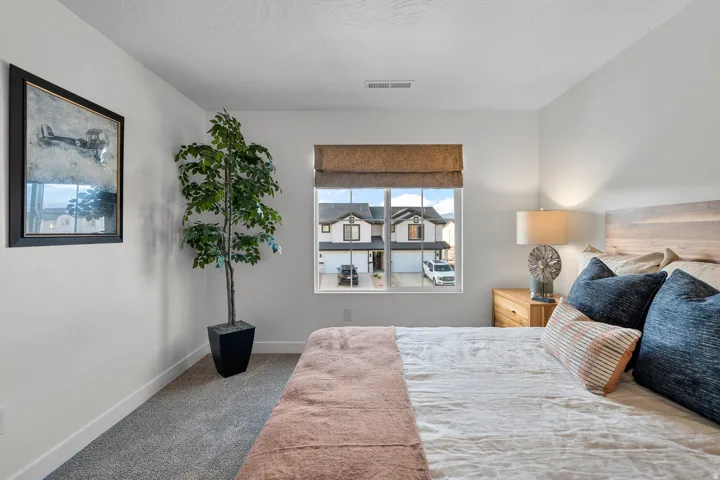Carpeted bedroom with a single window featuring a woven roman shade