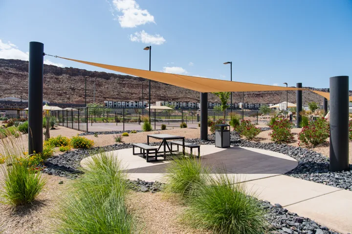 Outdoor recreational area featuring a shade sail structure, concrete pathways, and a picnic table