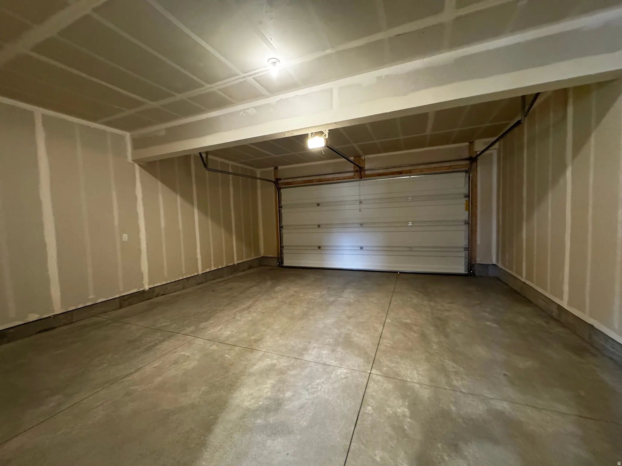 Spacious garage featuring a sectional overhead door, concrete flooring, and exposed ceiling joists