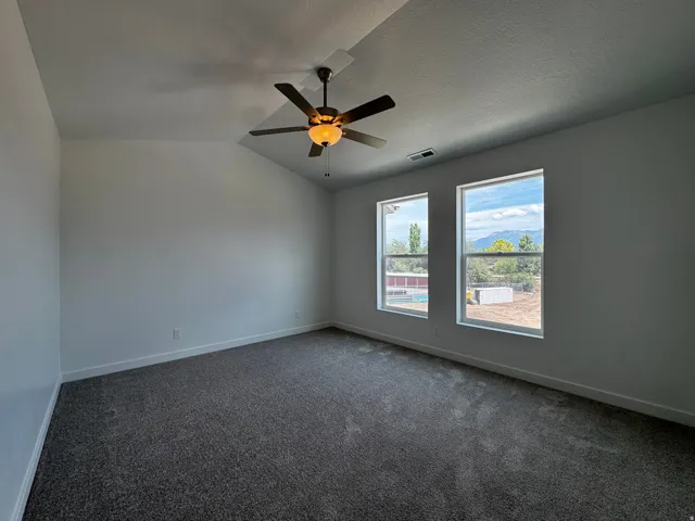 Room featuring a vaulted ceiling with a ceiling fan, two large windows, and wall-to-wall carpeting