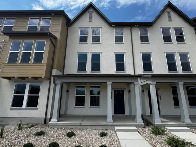 Multi-story townhome featuring a neutral stucco exterior, prominent bay window with horizontal siding, and an inviting covered porch