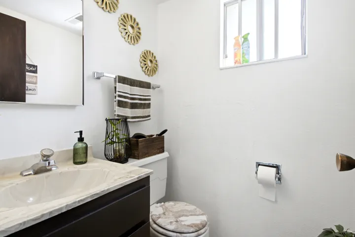 Bathroom featuring a vanity with a light-toned countertop and dark cabinetry, an integrated sink, a wall-mounted mirror, and a window providing natural light