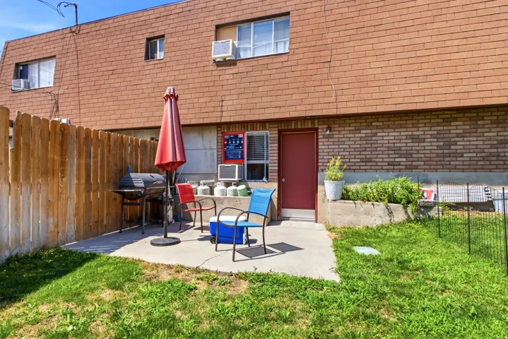 Rear concrete patio with a red entry door, framed by a wooden privacy fence, and featuring a brick exterior facade