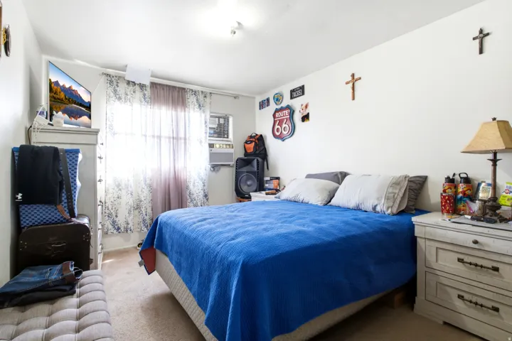 Bedroom featuring carpet flooring, a window with sheer and patterned curtains, white walls, and a ceiling-mounted light fixture