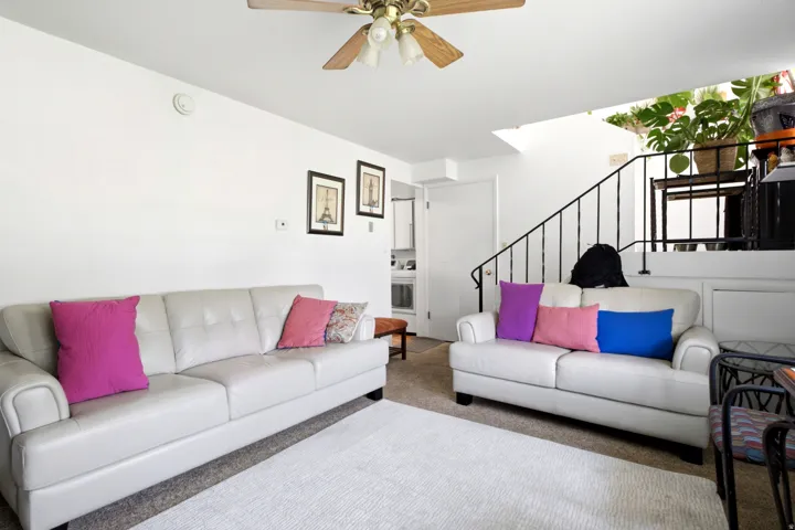 Living area featuring a ceiling fan with light fixture, white walls, and carpet flooring