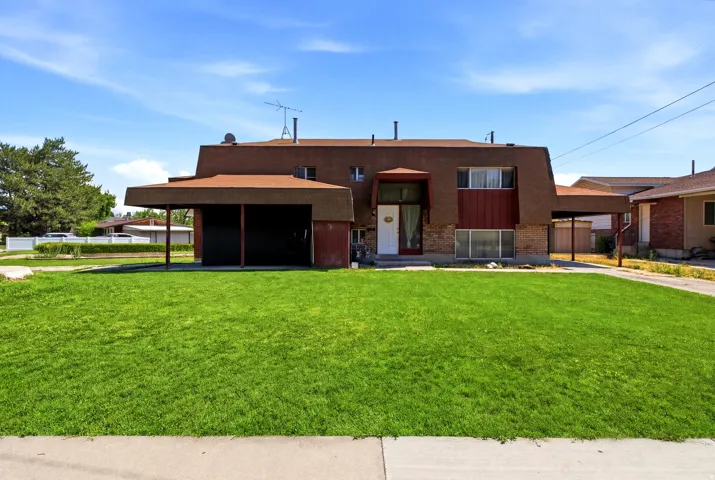 Brown multi-level exterior featuring a prominent carport, a paved driveway, and a front entry with a white door
