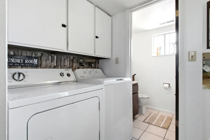 Dedicated laundry area featuring white cabinetry with dark hardware and a stone-look backsplash