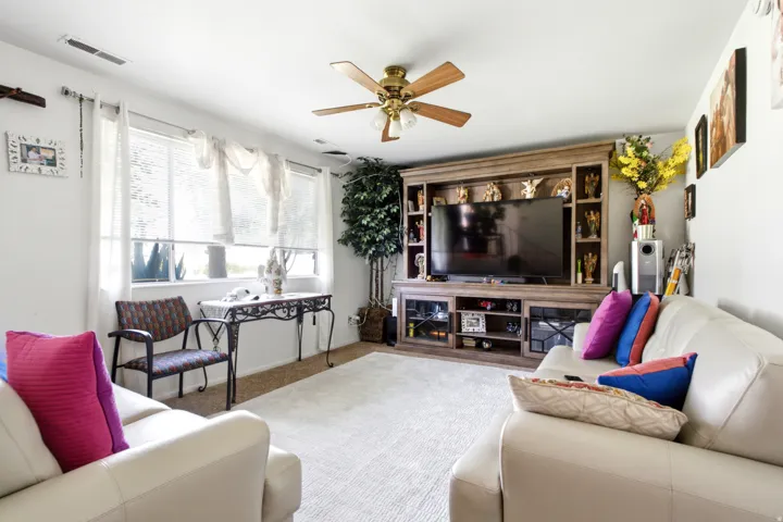 Living area featuring a ceiling fan with light fixture, multiple windows, and light-toned carpet flooring