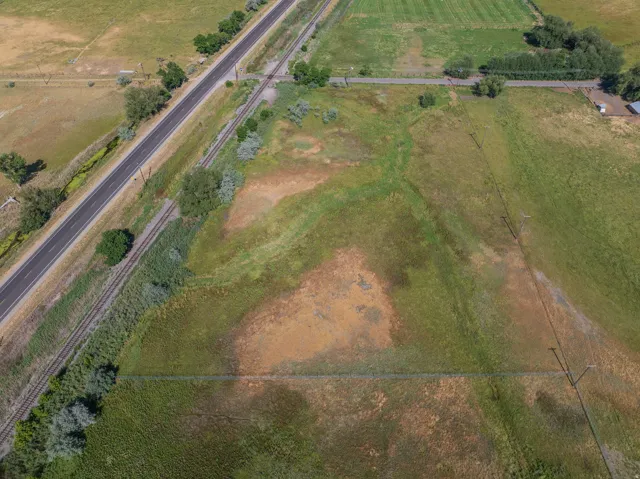 Expansive agricultural land featuring a paved road, railroad tracks, and natural vegetation
