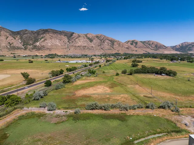 Expansive rural landscape featuring a paved road, scattered green fields, and distant mountainous terrain