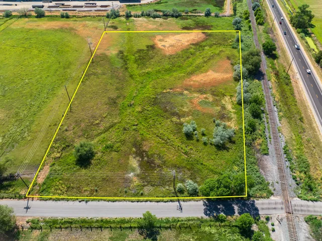 Expansive lot featuring varied ground cover, bordering a paved road, and adjacent to railway lines