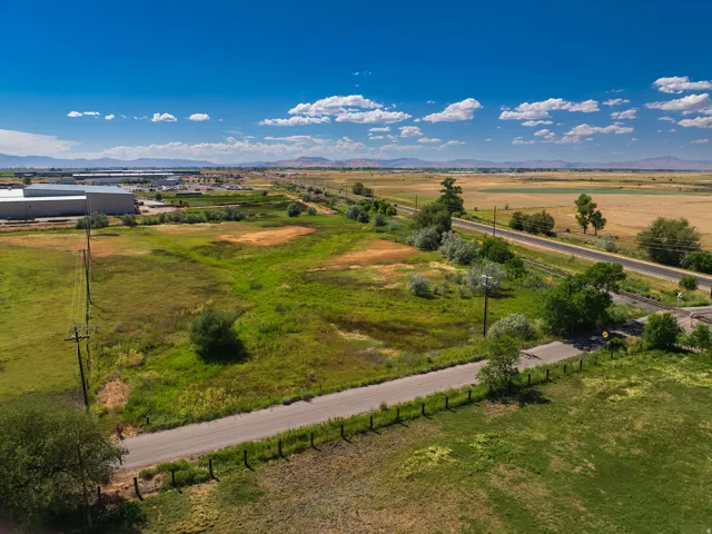 Expansive land parcel featuring a paved road, a clear blue sky, and distant mountain ranges