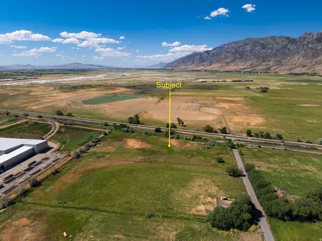 Expansive rural landscape featuring a prominent mountain range backdrop, a visible roadway, and significant open land