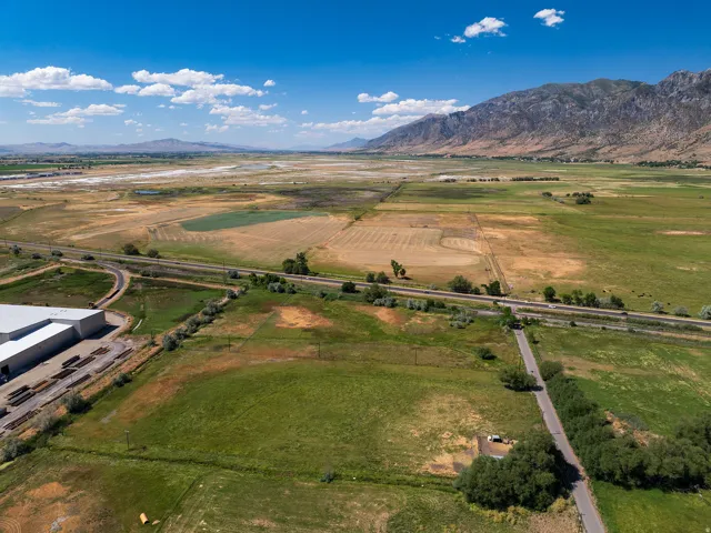 Expansive agricultural land featuring a paved road, a commercial building with a gray roof, and distant mountains under a clear sky