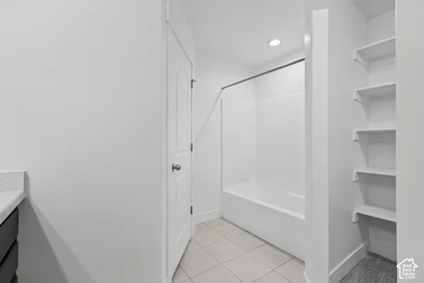 White subway tile flooring, built-in shelving, recessed lighting, and a white tub with shower