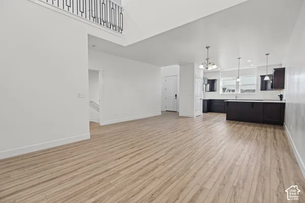 Open-concept main living area with wood-finish flooring, a two-story ceiling, and a kitchen featuring dark cabinetry, white countertops, and pendant lighting