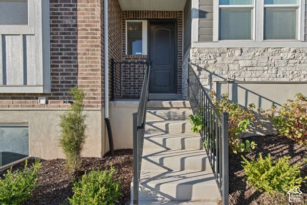 Brick and stone facade with a dark entry door, concrete steps, and black metal railings