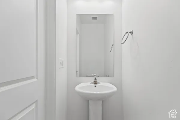 Pedestal sink with chrome faucet, rectangular mirror, and a wall-mounted towel ring