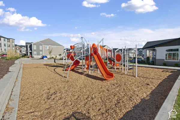 Community playground featuring multiple elevated play structures with tube slides, climbing elements, and interactive components set on engineered wood fiber surfacing