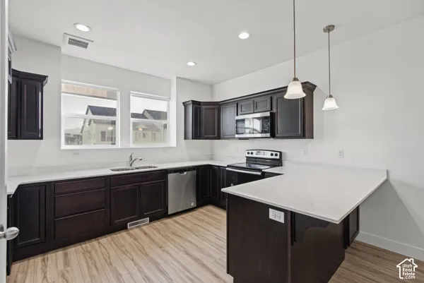 Modern kitchen with dark wood-finish cabinetry, light stone countertops, stainless steel appliances, and wood-finish flooring