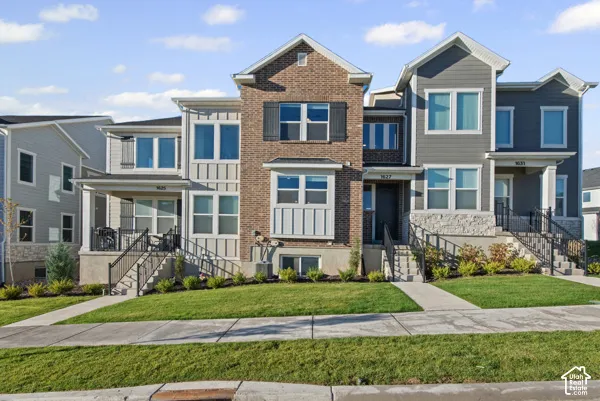 Contemporary townhome with a brick and siding exterior, featuring multiple windows, a covered porch, and a manicured lawn